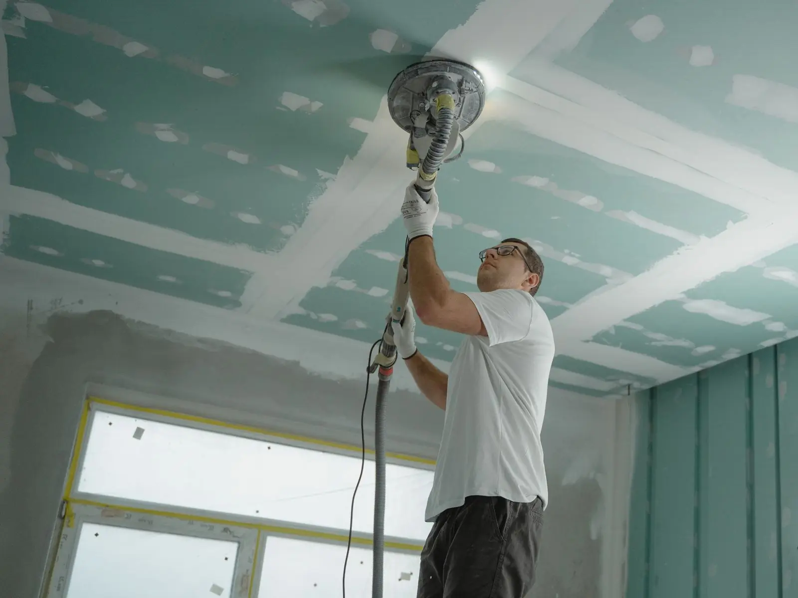 Worker sanding a drywall ceiling during repair work